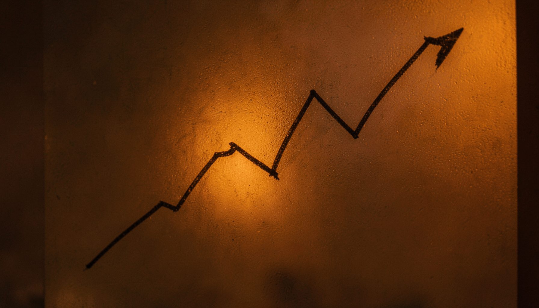 A downward-trending line graph sketched on frosted glass, lit by dim amber light, suggesting a gradual decline.