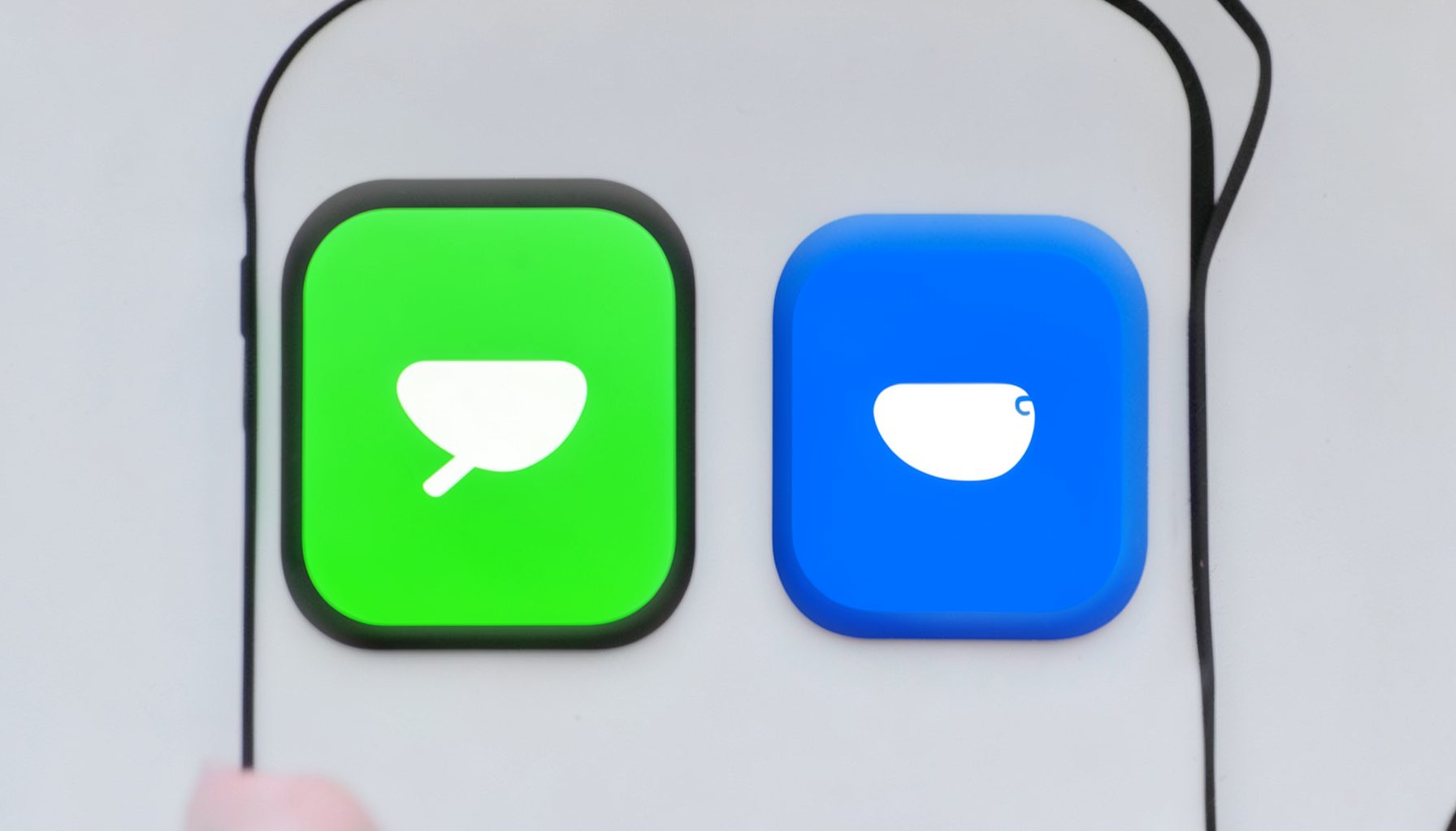Two app icons side by side on a smartphone screen, one green and one blue, under neutral daylight.