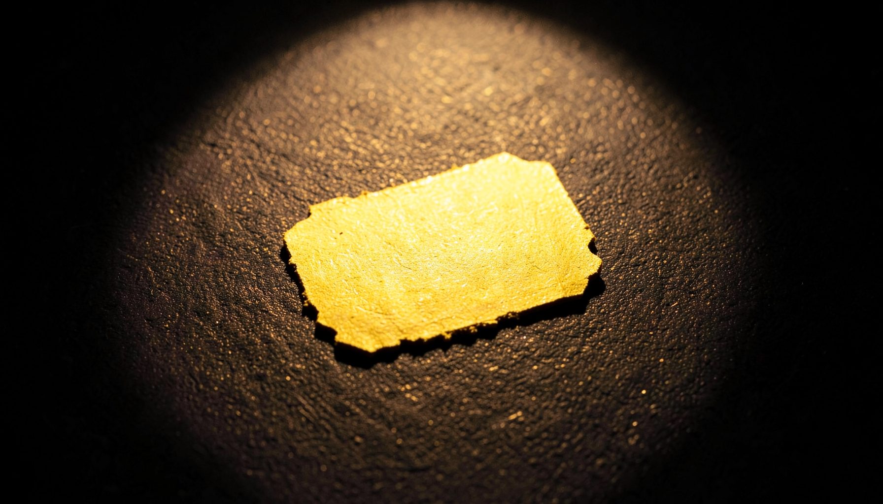 A golden ticket stub resting on a dark textured surface, illuminated by a single warm spotlight.